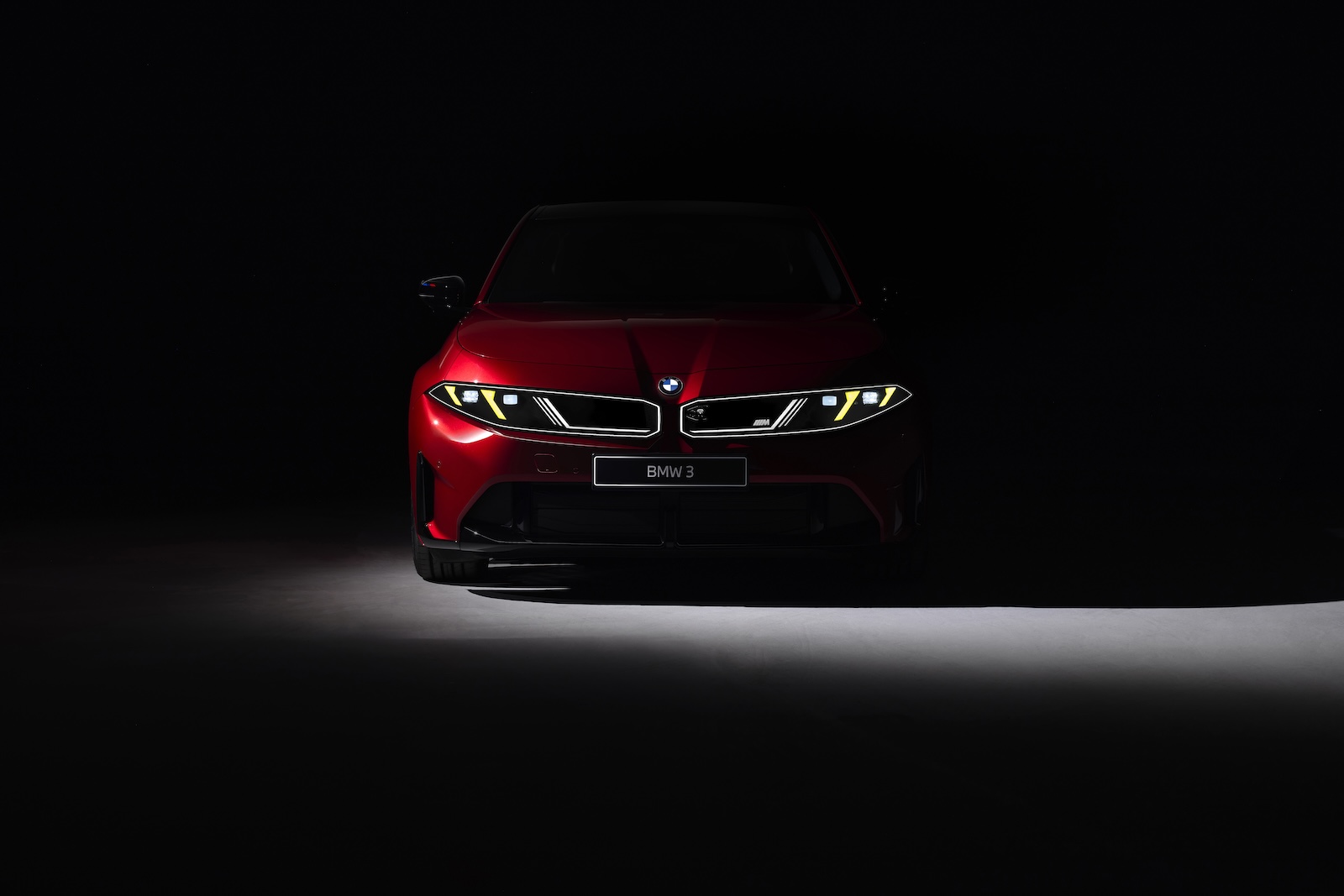 Czerwone BMW widziane z przodu, częściowo oświetlone na ciemnym tle.