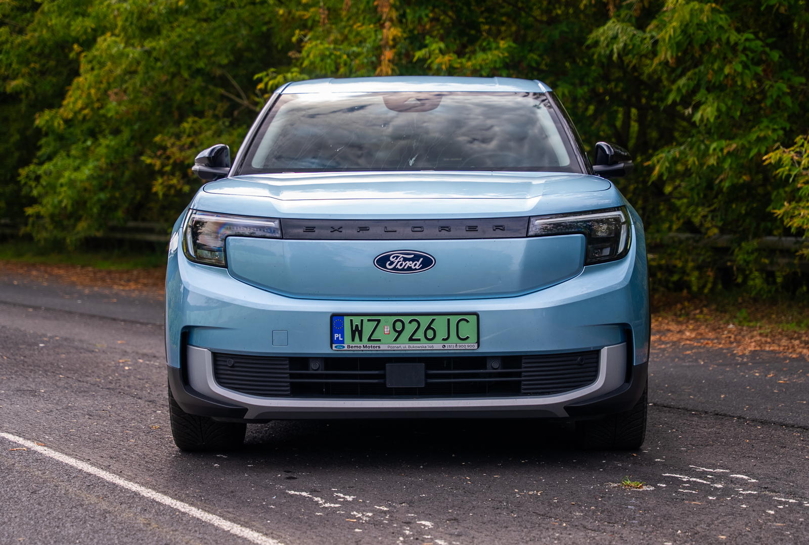 Niebieski, używany Ford Explorer EV stoi na drodze, a w tle widać zielone drzewa.