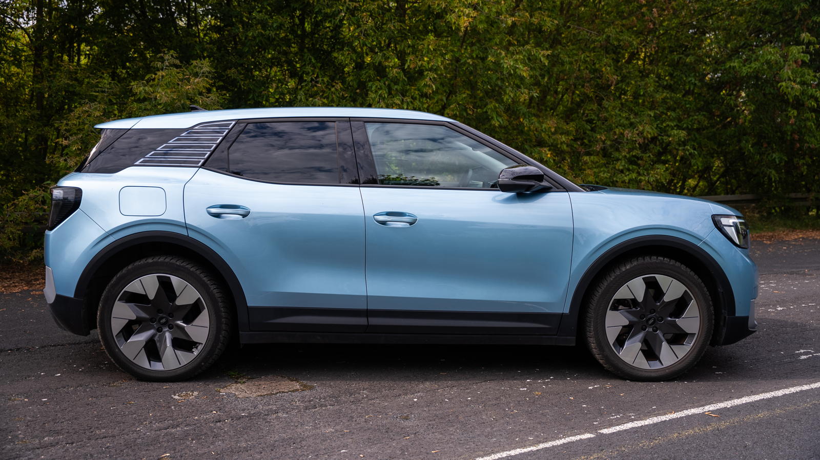 Niebieski SUV, prawdopodobnie używany Ford Explorer EV, stoi na chodniku przy zielonych drzewach.