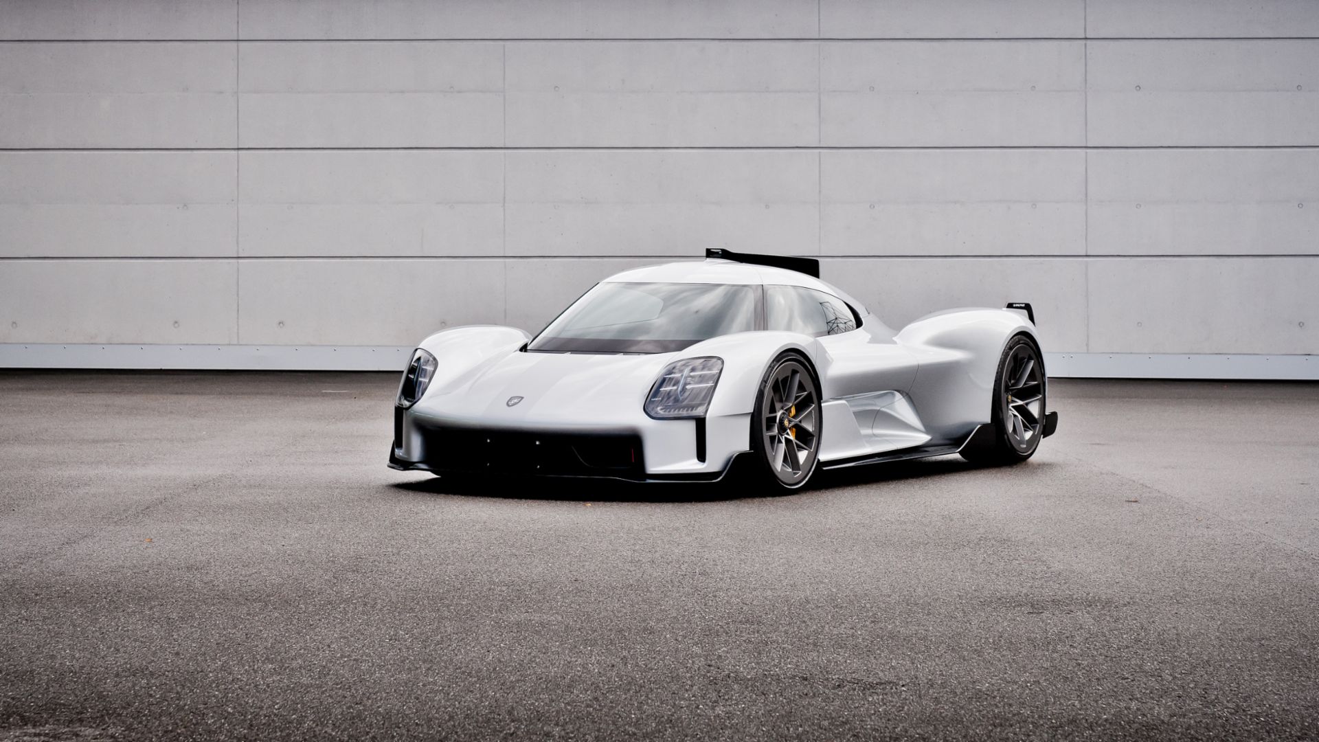 Białe sportowe Porsche stoi na szarym asfalcie przed dużą, gładką białą ścianą.