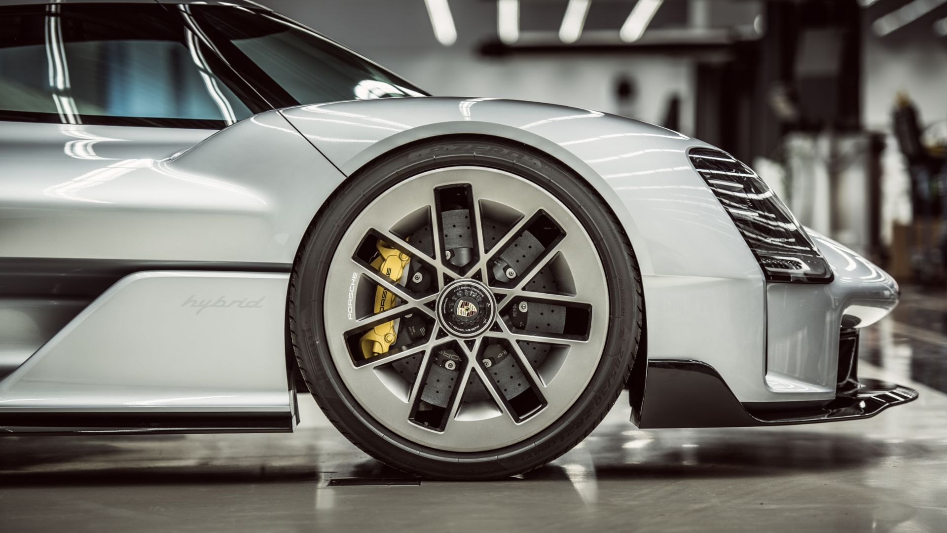 Przednie lewe koło i nadkola srebrnego Porsche; widoczny zacisk hamulca i reflektor.