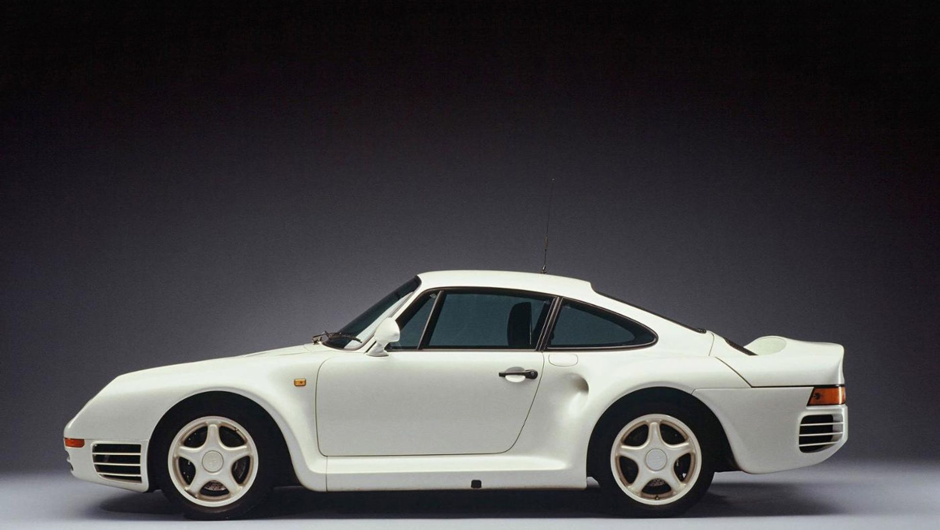 Białe, klasyczne sportowe Porsche widziane z profilu na ciemnym tle z efektem gradientu.