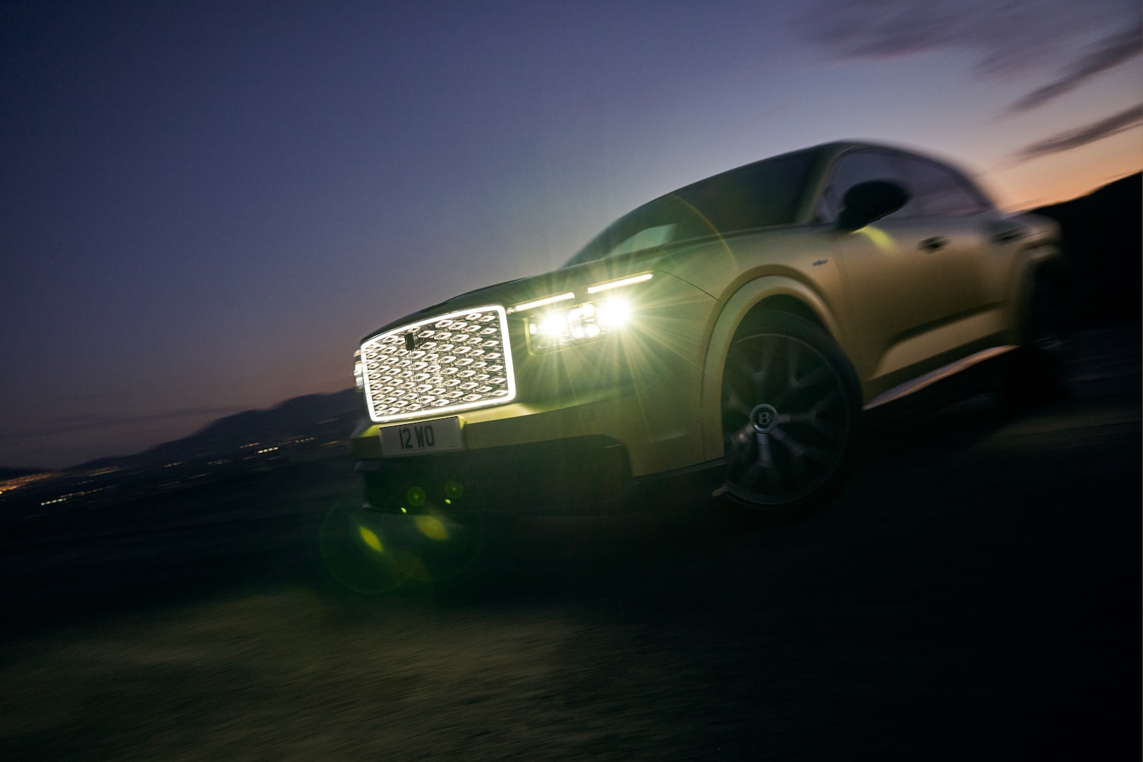 Rozmazany Bentley z włączonymi światłami i podświetloną atrapą chłodnicy o zmierzchu.
