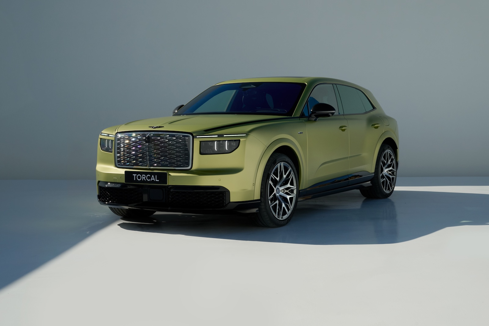 Jasnozielony SUV marki Bentley Torcal stoi w pomieszczeniu na białej podłodze, na szarym tle.