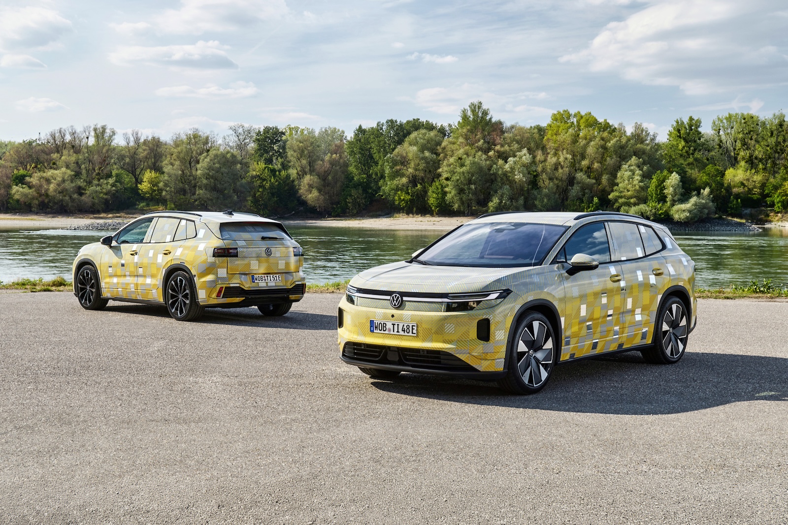 Dwa zamaskowane elektryczne SUV-y marki Volkswagen, w tym model ID. Tiguan, stojące nad rzeką.
