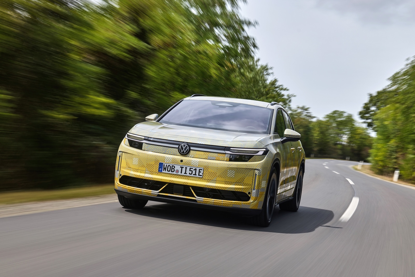 Żółty Volkswagen ID. SUV na zakręcie pośród zieleni pod pochmurnym niebem.
