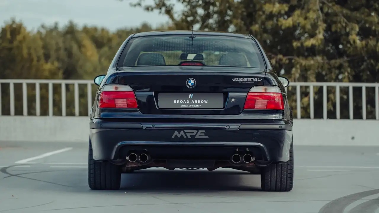 Czarny sedan BMW z czterema rurami wydechowymi, szerokimi oponami i napisem MPE.