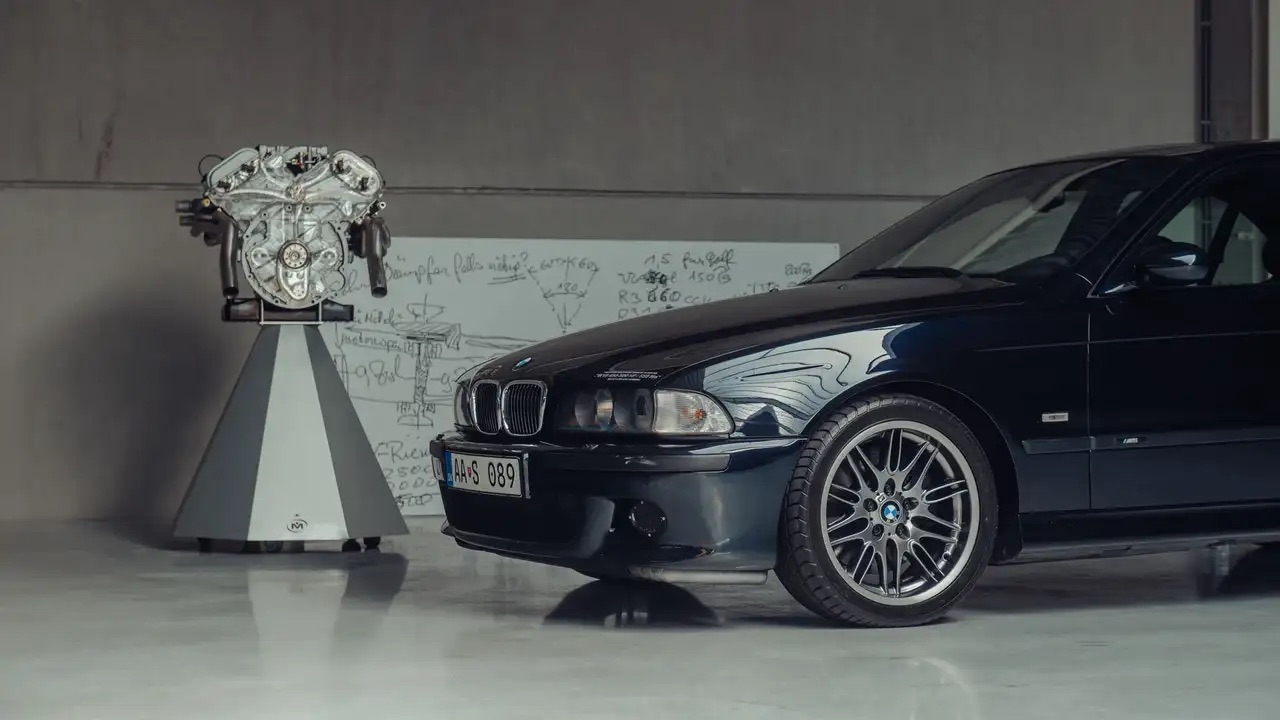 Ciemny sedan marki BMW stoi obok dużego silnika i tablicy z schematami technicznymi.