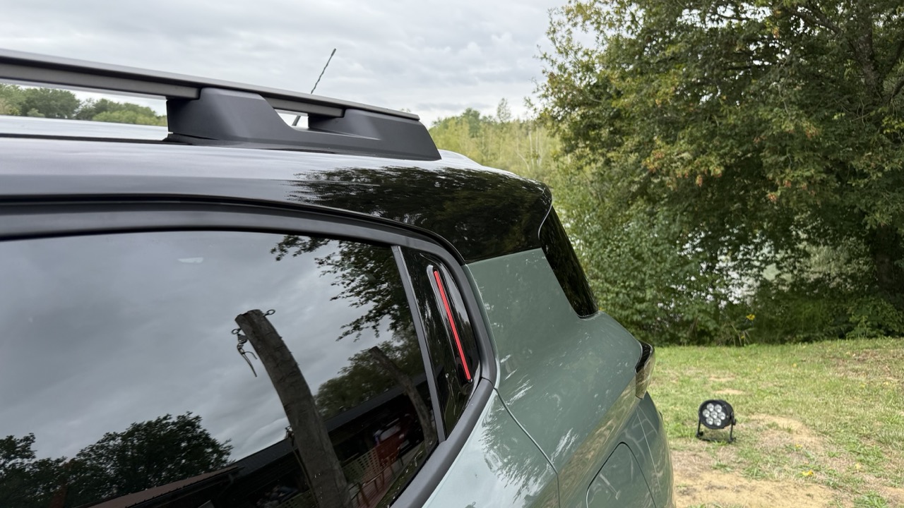Zielony SUV z czarnym dachem i bagażnikiem, zaparkowany na trawie przy drzewach.