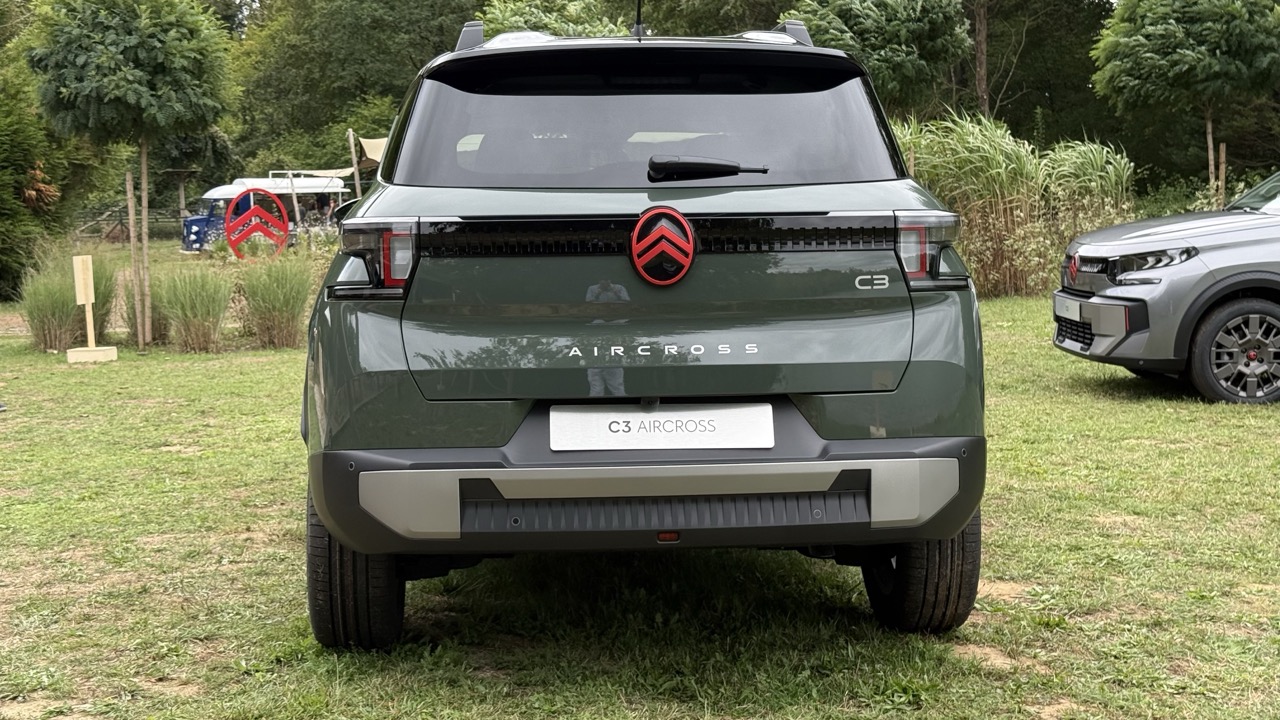 Zielony Citroën C3 Aircross widziany od tyłu, zaparkowany na trawie pośród zieleni i innych samochodów.