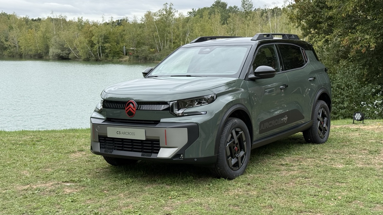 Zielony Citroën C3 Aircross stoi na trawie nad jeziorem, a w tle widać drzewa i chmury.