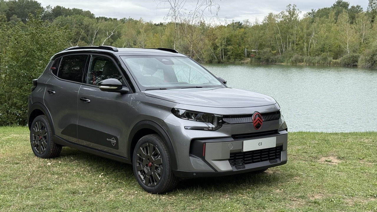 Szary Citroën C5 Aircross stoi na trawie nad jeziorem, a w tle widać drzewa i chmury.