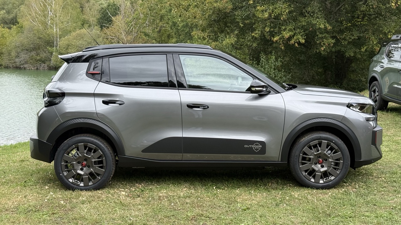 Szary, kompaktowy SUV stoi na trawie nad wodą, a w tle widać drzewa.
