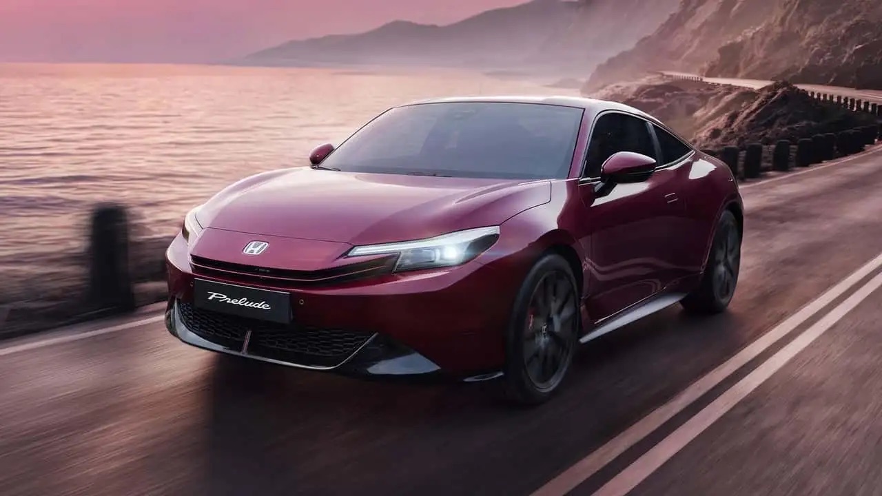 Czerwona Honda Prelude na nadmorskiej drodze o zachodzie słońca, z klifami i oceanem w tle.