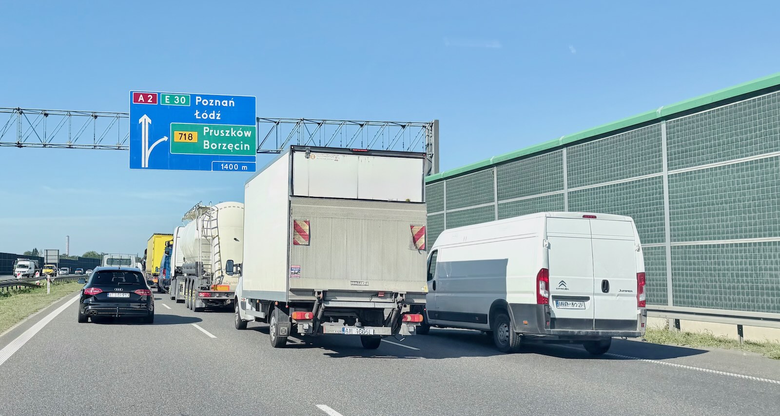 Samochody i ciężarówki stoją w korku przy znaku wskazującym kierunek do Poznania, Łodzi, Pruszkowa i Borzęcina.