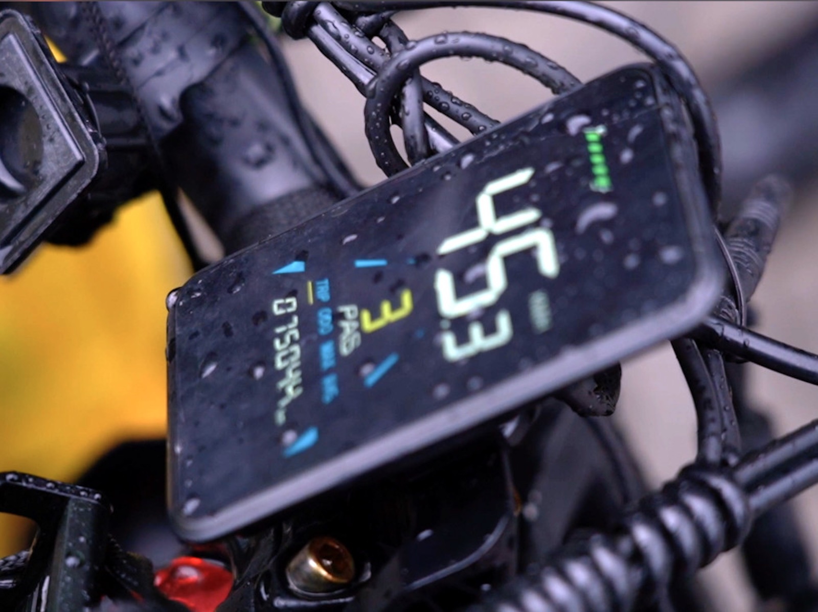 Zbliżenie na wyświetlacz prędkościomierza roweru wskazujący 45,3 km/h, z kroplami deszczu.