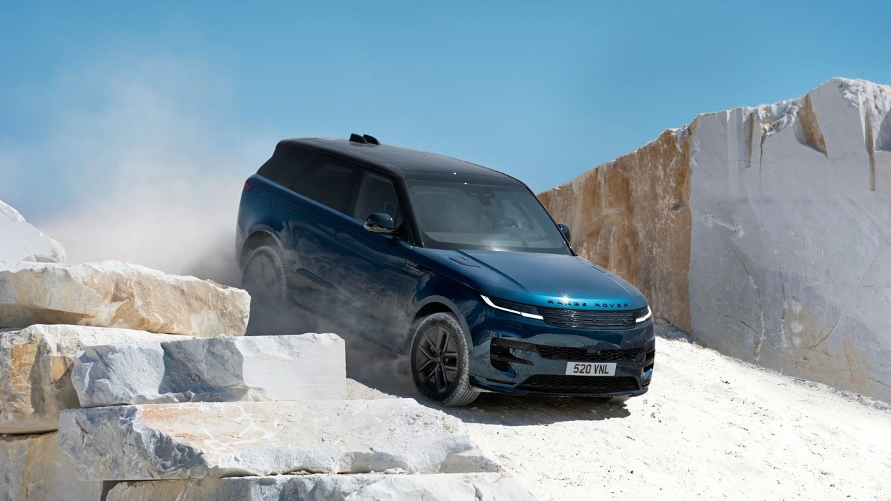 Niebieski Range Rover zjeżdża po skalistym, piaszczystym zboczu między białymi blokami kamieni.