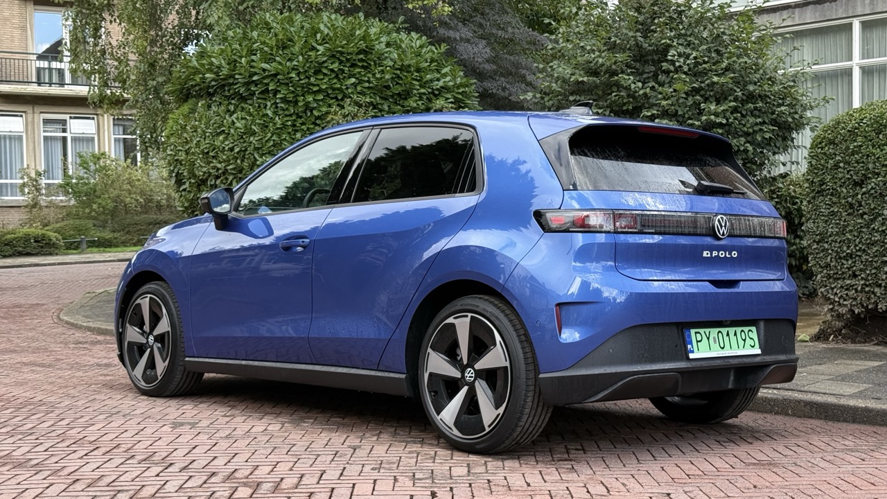 Niebieski Volkswagen ID.2all stoi na brukowanej drodze obok zielonych krzewów i budynków.