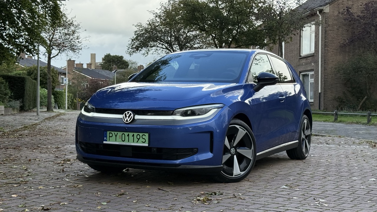 Niebieski Volkswagen stoi na brukowanej drodze pośród domów i drzew.