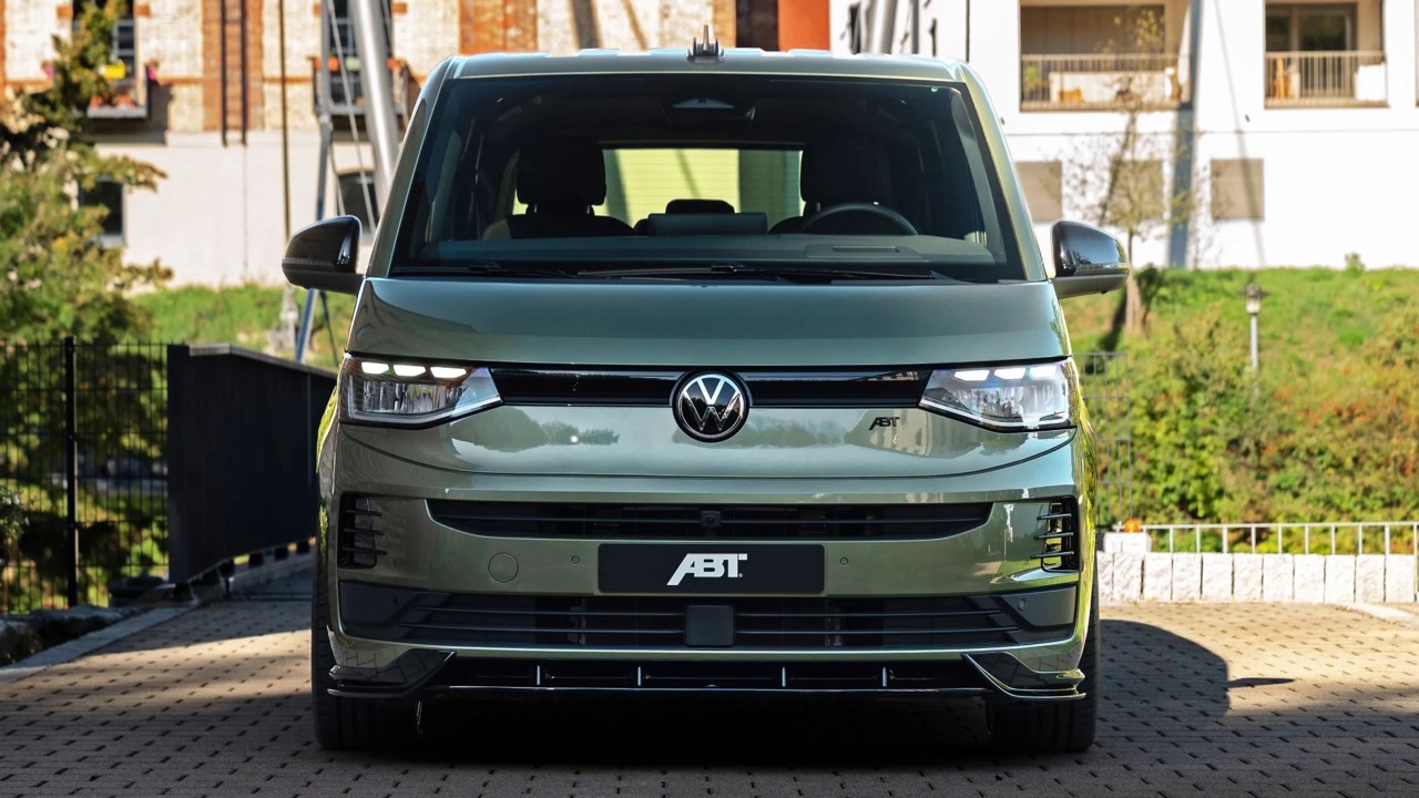 Zielony Volkswagen ABT widziany z przodu, stojący na kostce brukowej przed budynkami i zielenią.