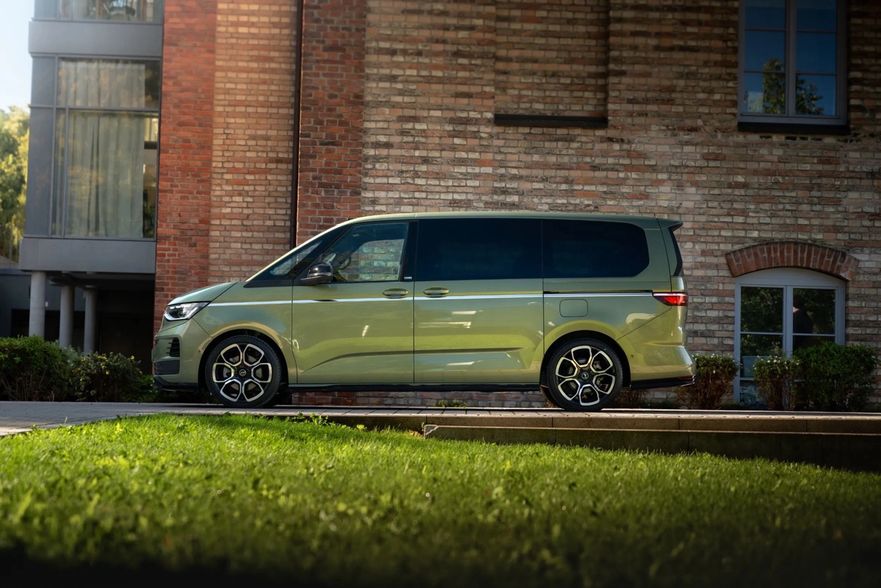 Zielony minivan stoi przed ceglanym budynkiem z dużymi oknami i zielenią przed nim.