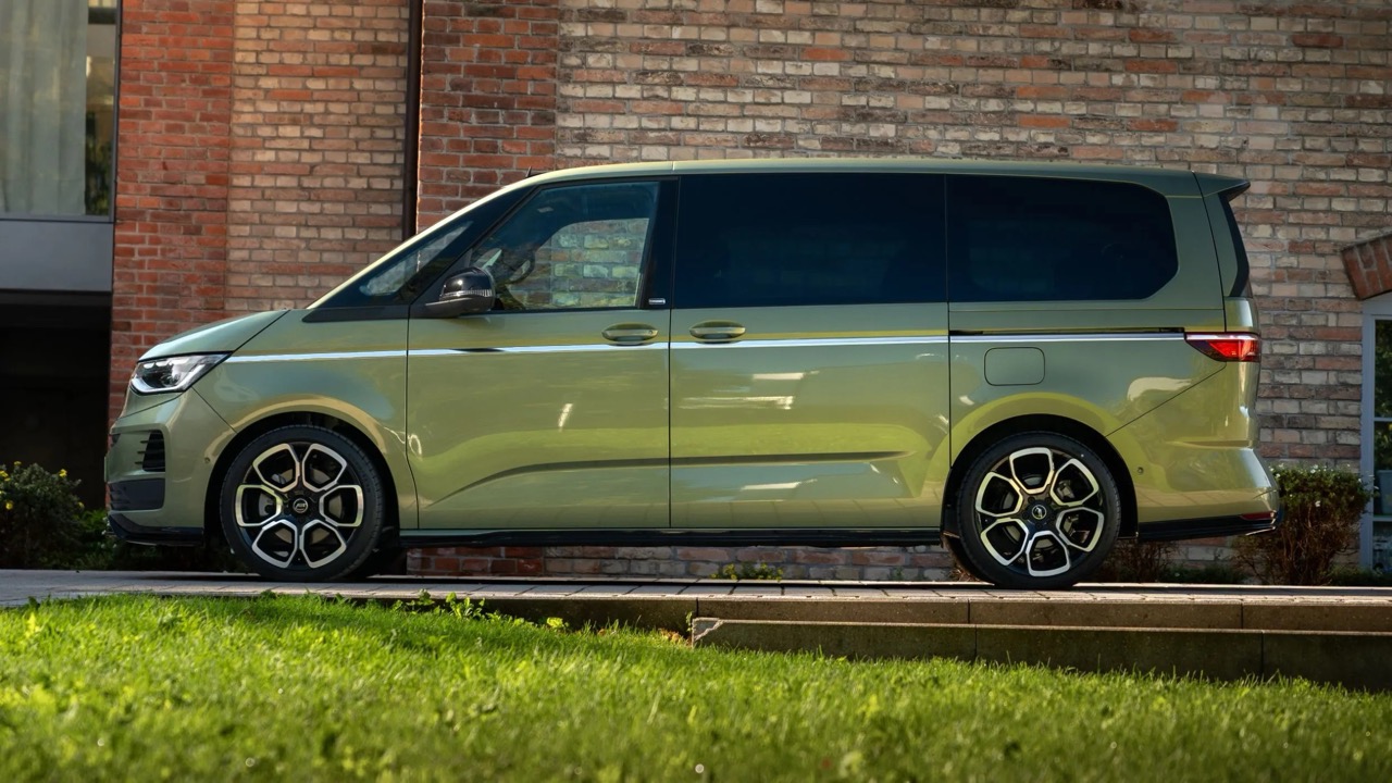 Zielony minivan stoi na podjeździe przy ceglanej kamienicy, z przodu widać trawę, świeci słońce.