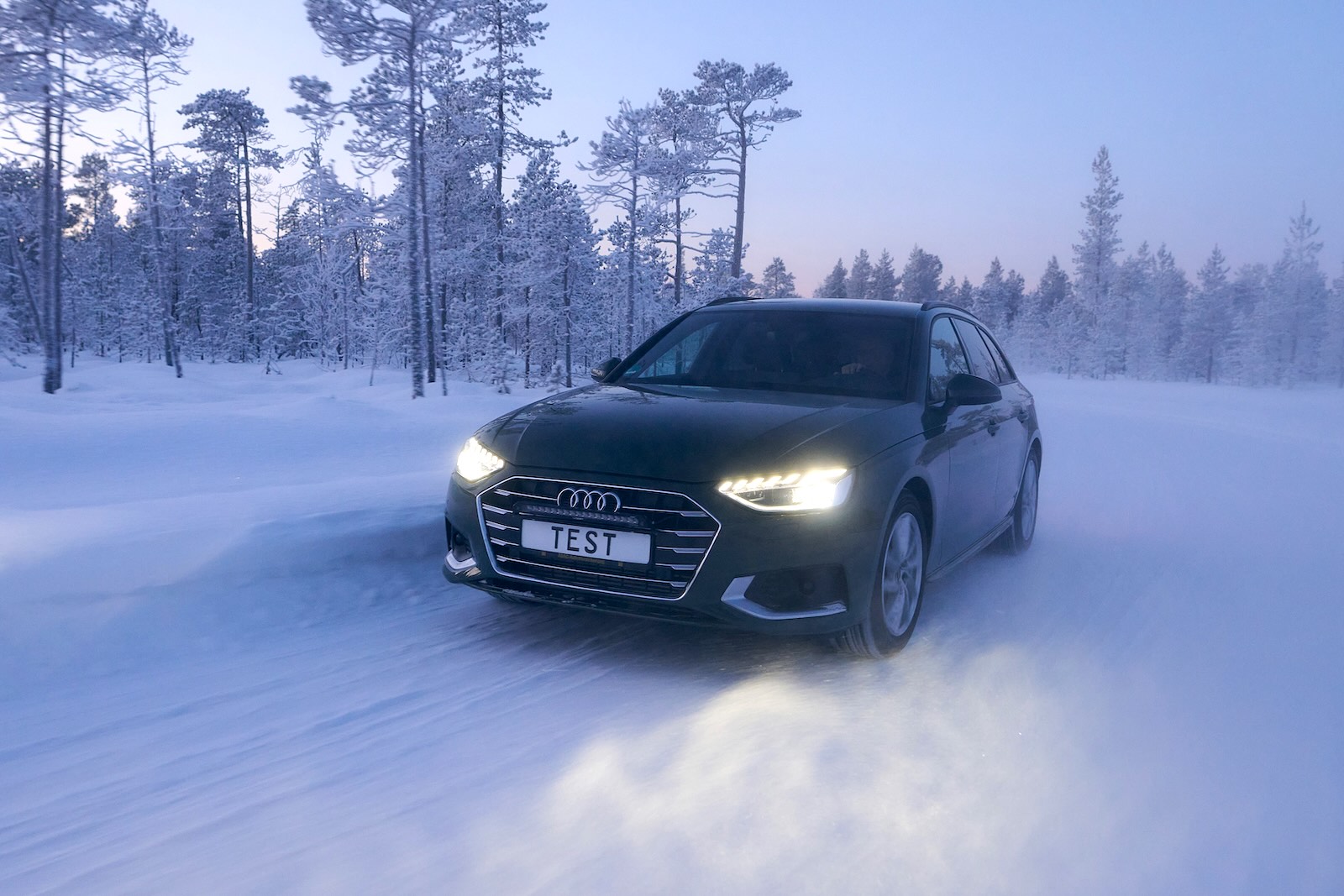 Czarne Audi na śliskiej, zaśnieżonej drodze; tabliczka z napisem „TEST”, zużyte opony zimowe.