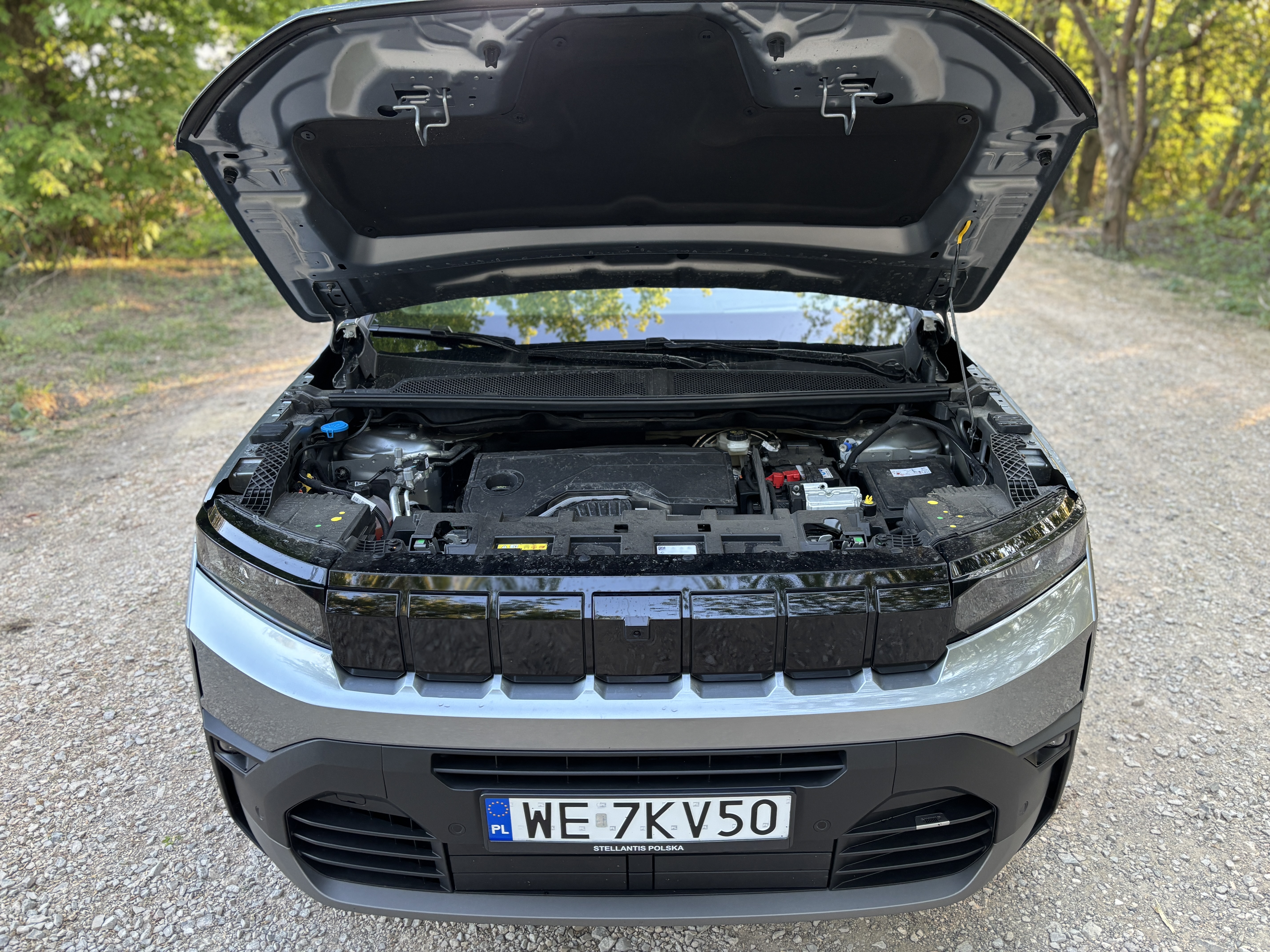 Srebrny SUV z otwartą maską i widocznym silnikiem.