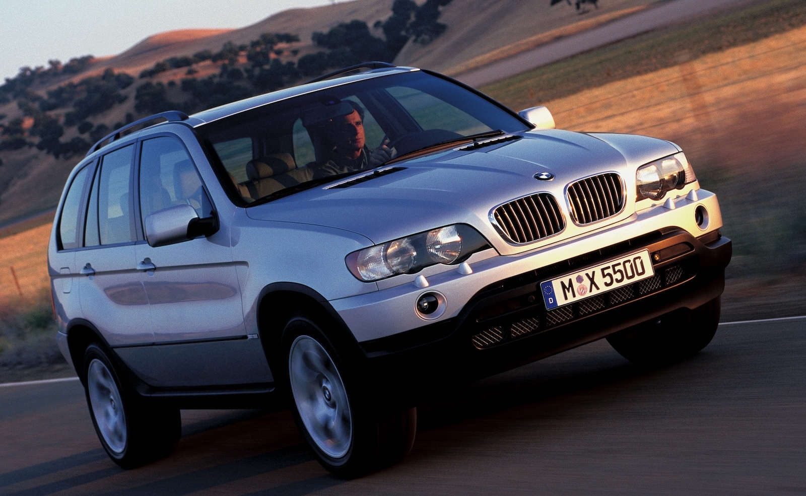 Srebrne BMW X5 jadące drogą.