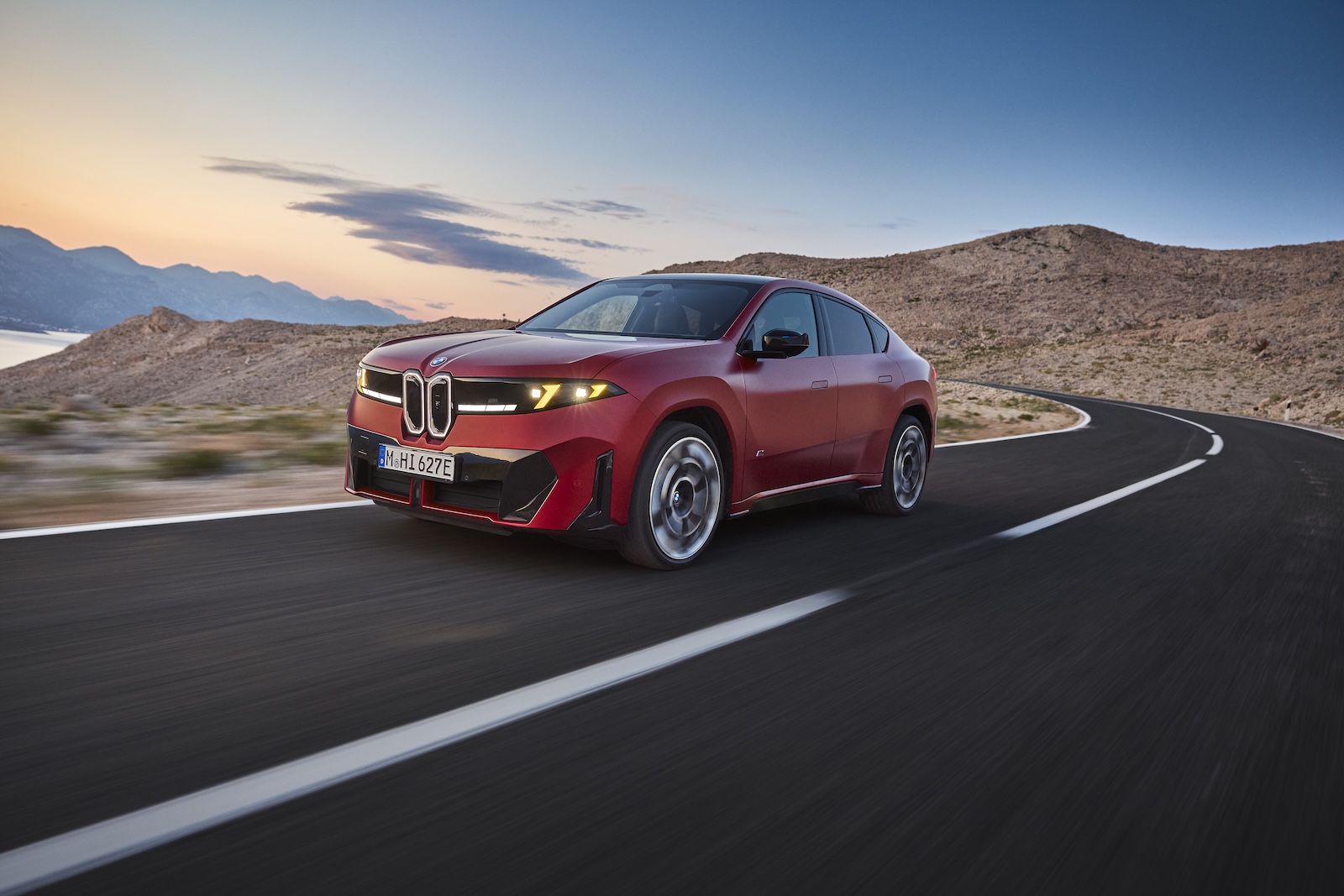 Czerwone BMW XM i iX4 jadące przez pustynię o zachodzie słońca.