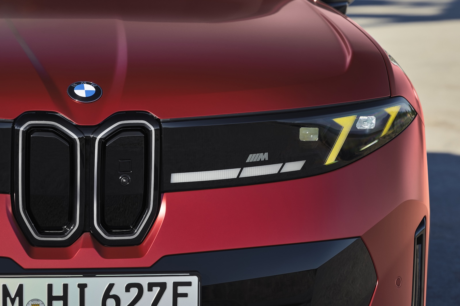 Przód czerwonego BMW iX4 z logo, reflektorem i emblematem M.