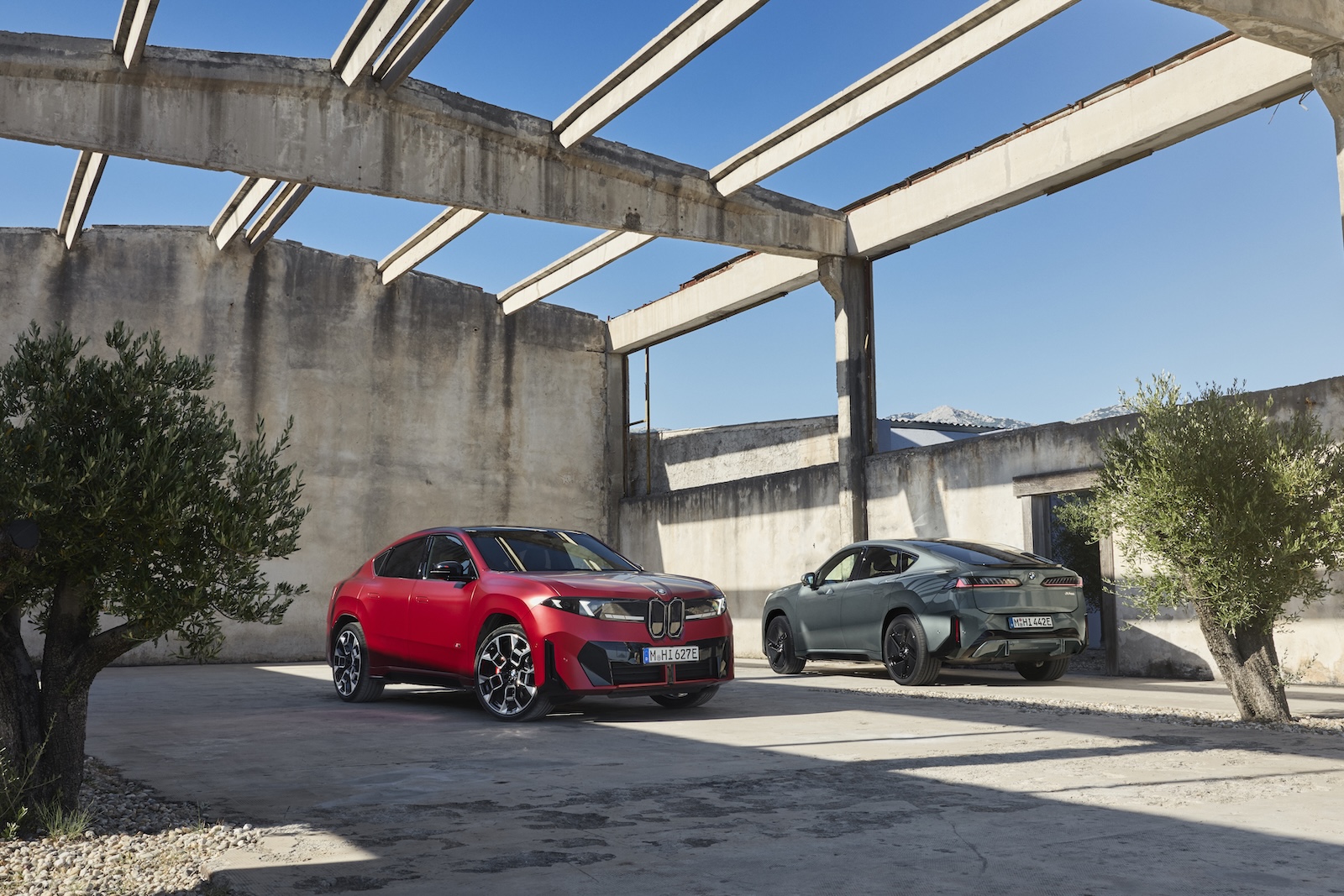 Czerwone i szare BMW iX2 oraz iX4 zaparkowane w betonowej konstrukcji.