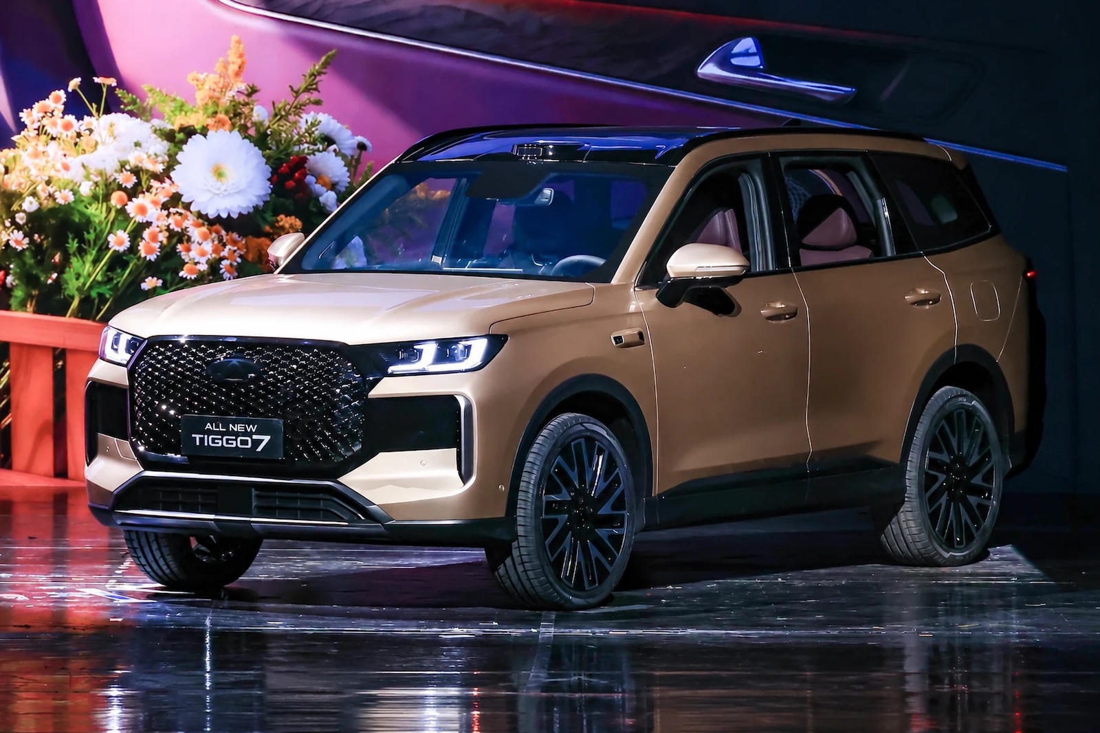 Złoty SUV Tiggo 7 na wystawie z kwiatową dekoracją w tle.