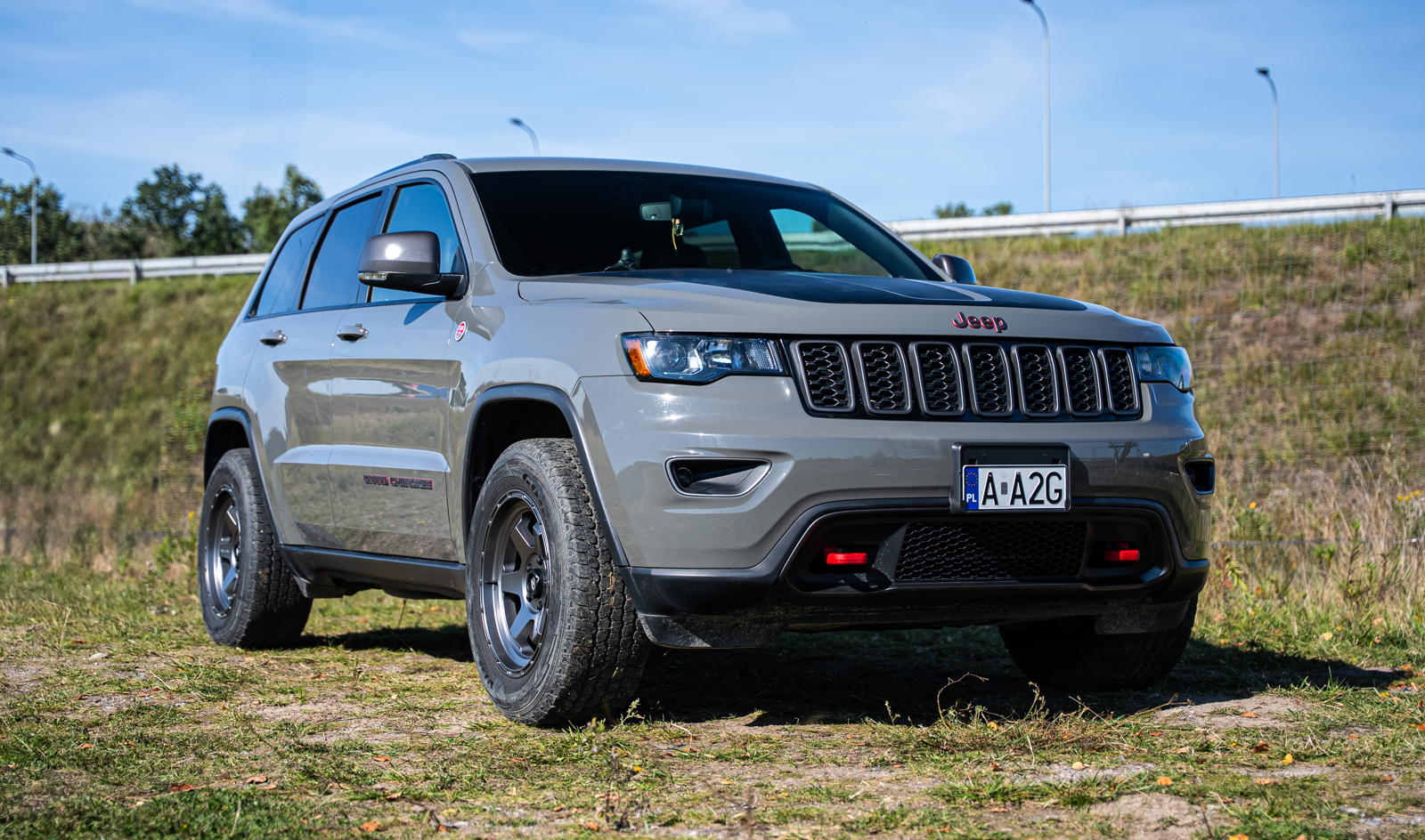 Szary Jeep Grand Cherokee WK2 zaparkowany na trawiastym poboczu.