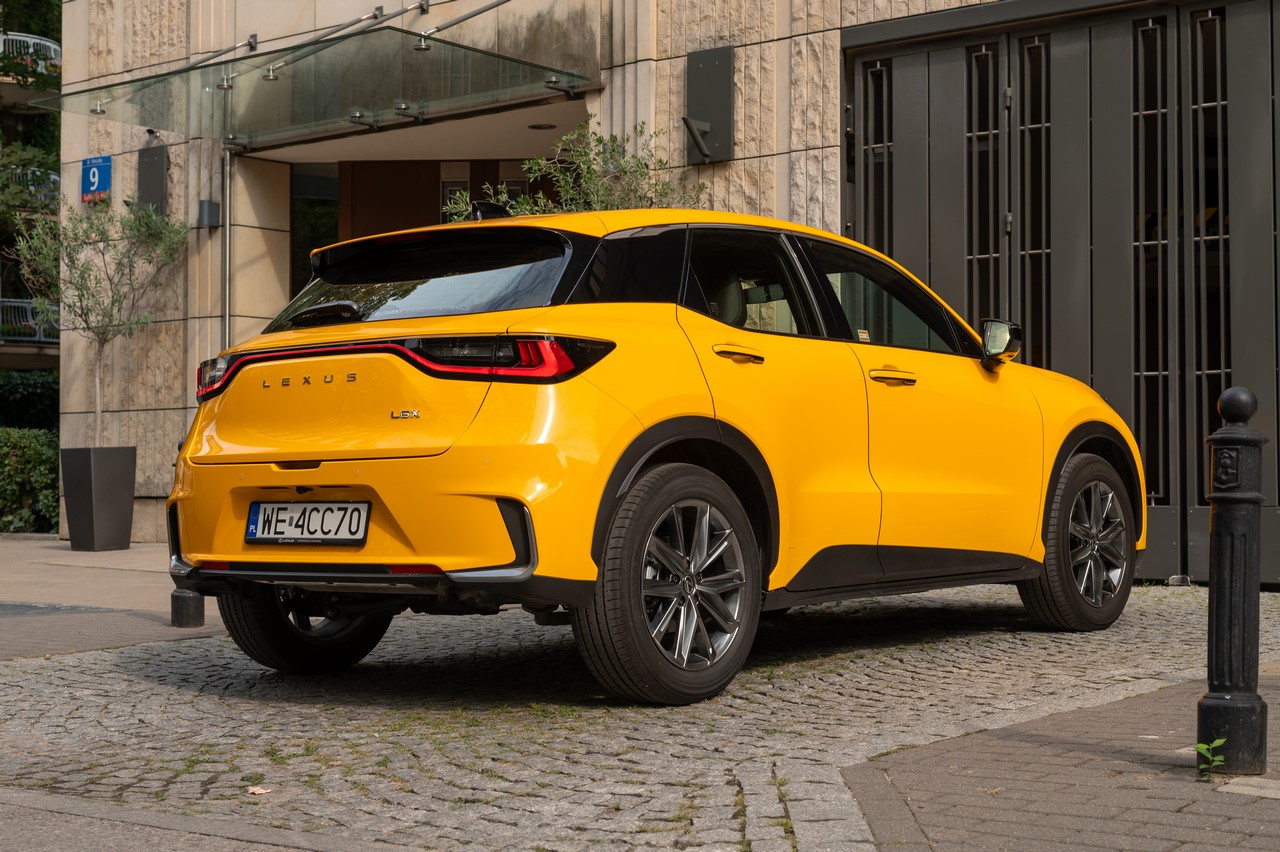 Żółty Lexus LBX zaparkowany na brukowanym podjeździe przed budynkiem.