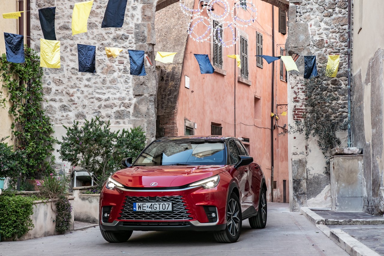 Czerwony Lexus LBX jadący wąską, brukowaną uliczką starego europejskiego miasta.