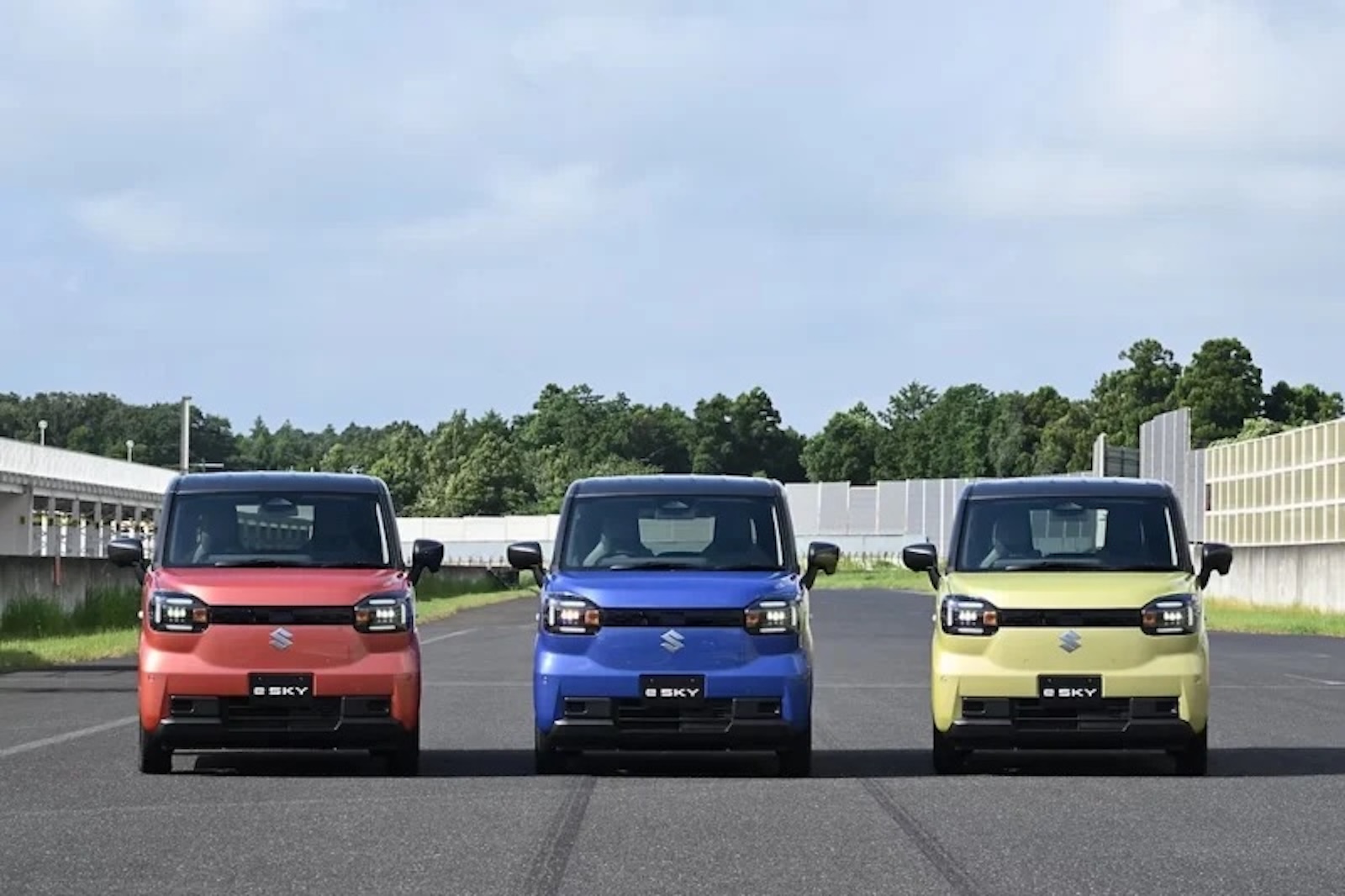 Pomarańczowe, niebieskie i żółte Suzuki E-Sky zaparkowane obok siebie na torze.