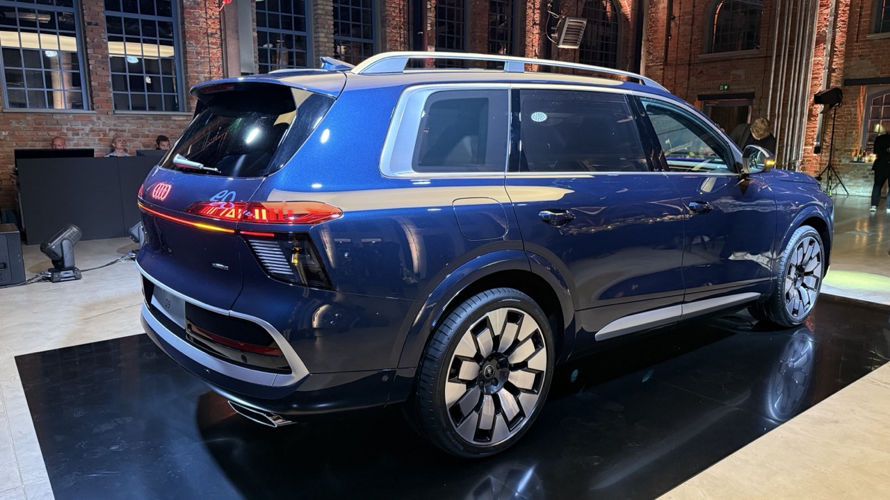 Niebieski SUV marki Audi stoi na czarnej platformie w pomieszczeniu z ceglaną ścianą i dużymi oknami.