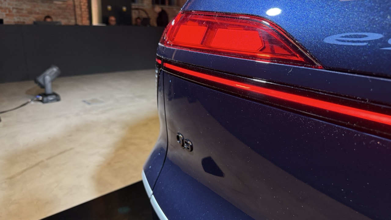 Tylny róg niebieskiego Audi e-tron, światła i logo w słabo oświetlonym wnętrzu.
