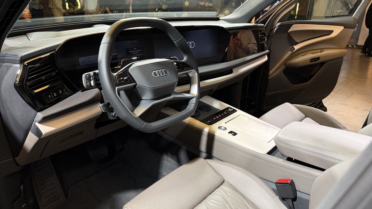 Wnętrze Audi z cyfrowym kokpitem, dużą kierownicą, beżową tapicerką skórzaną i konsolą dotykową.