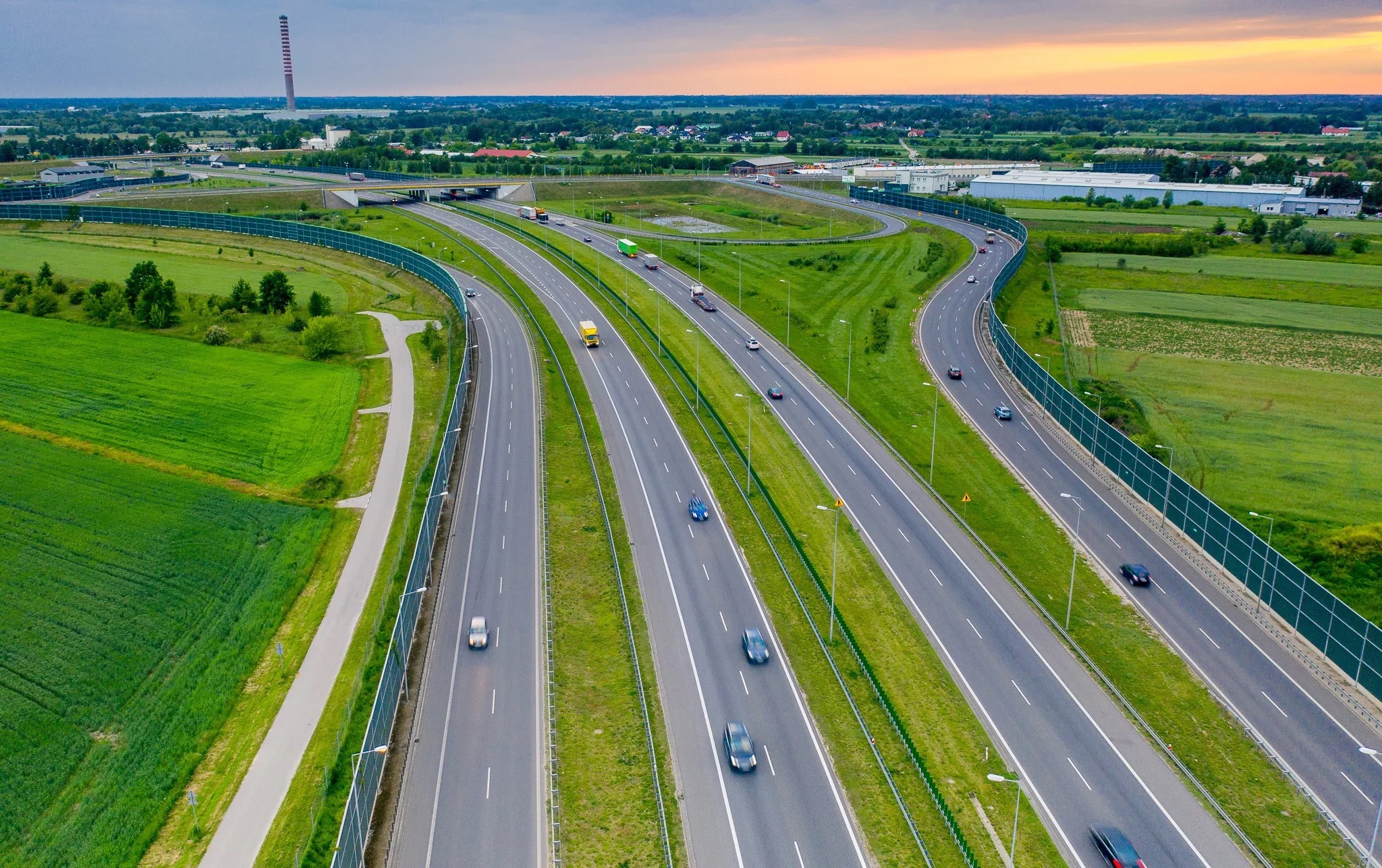 Wielopasmowa autostrada wśród zielonych pól o zachodzie słońca – widok z lotu ptaka.