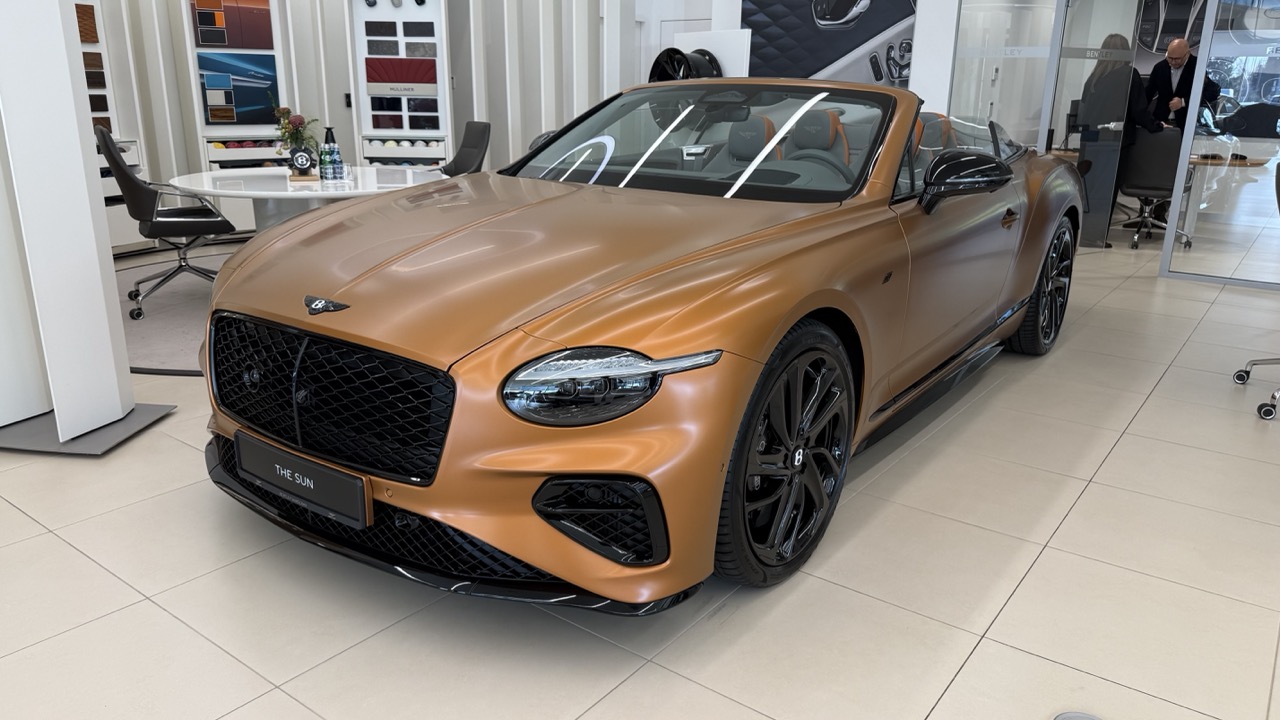 Miedziany kabriolet Bentley Continental GT zaparkowany w salonie.