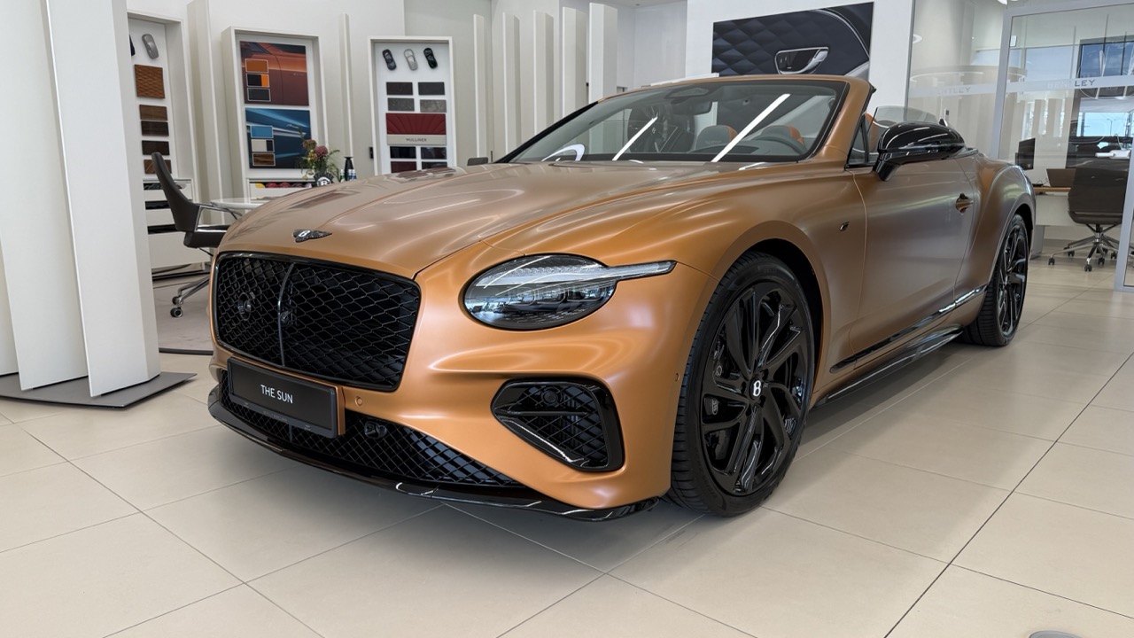 Miedziany kabriolet Bentley Continental GT zaparkowany w salonie samochodowym.