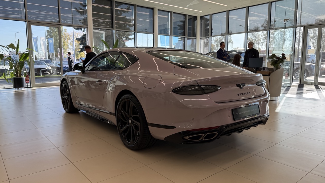 Jasnoróżowe coupe marki Bentley zaparkowane w salonie samochodowym.