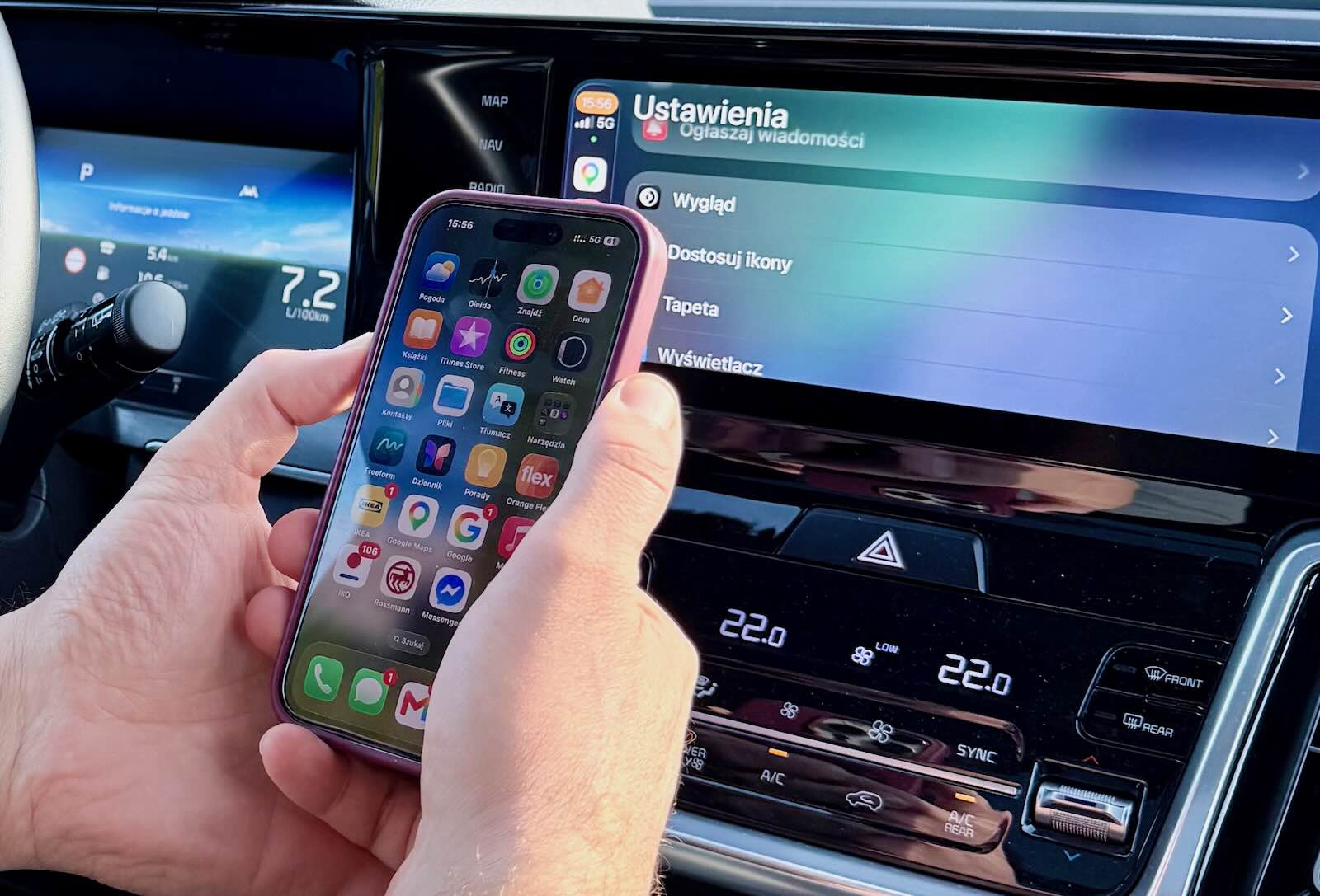 Osoba trzyma smartfon z aplikacjami przy desce rozdzielczej samochodu wyposażonego w Apple CarPlay w języku polskim.