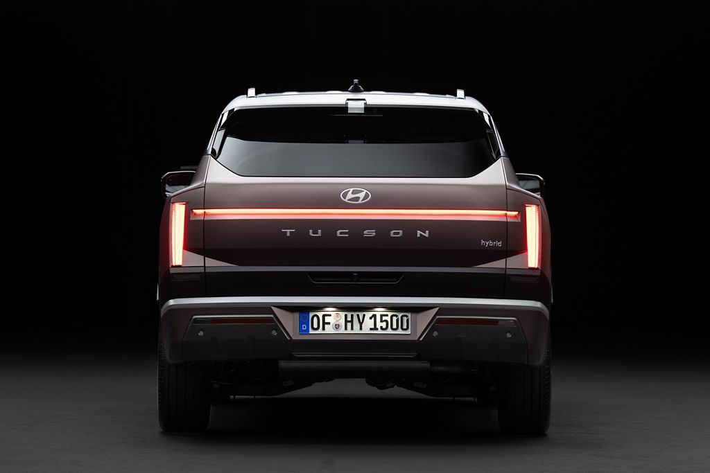 Tył czarnego Hyundaia Tucson Hybrid z włączonymi światłami i europejską tablicą rejestracyjną, na czarnym tle.