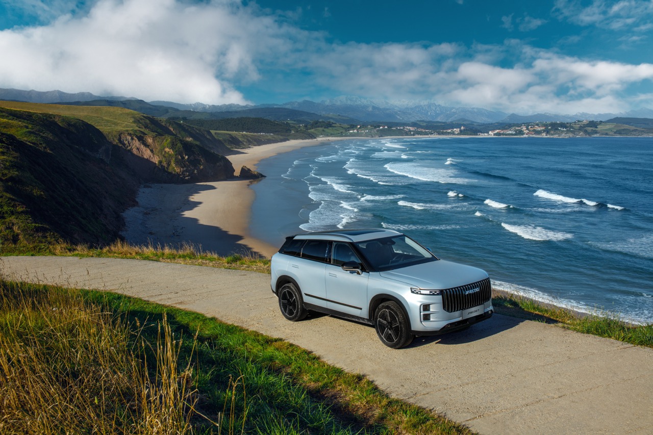 Srebrny SUV zaparkowany przy nadmorskiej drodze z widokiem na plażę i ocean.