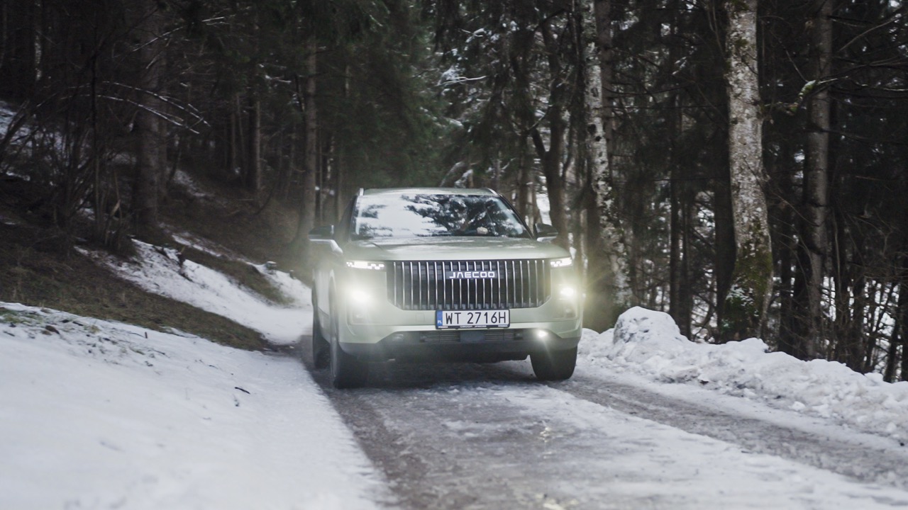 SUV marki Jaecoo jadący zaśnieżoną leśną drogą.