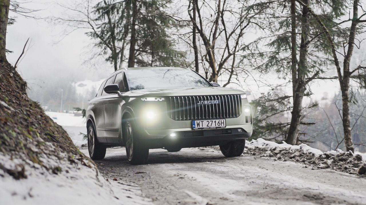 SUV marki Jaecoo jadący zaśnieżoną leśną drogą.