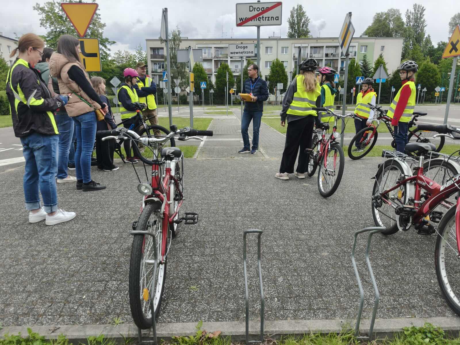 Instruktor i dzieci w kamizelkach odblaskowych przygotowujące się do lekcji bezpieczeństwa rowerowego.